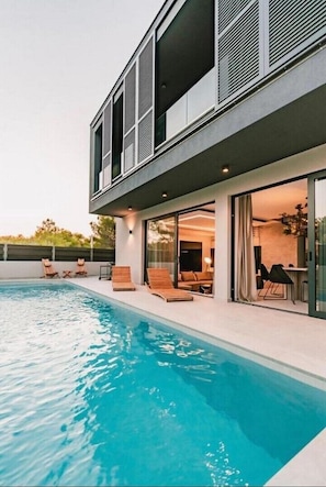 A modern house with a swimming pool, outdoor seating, and a large glass door leading to the interior. - Luxury Villa Hera in Vodice (Srima)