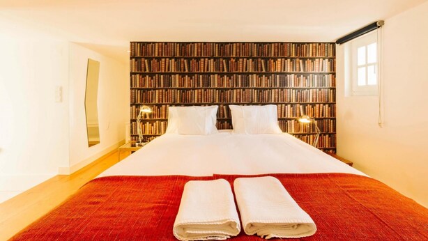 Una habitación de hotel con una cama grande, una pared de estanterías y dos lámparas de noche.
