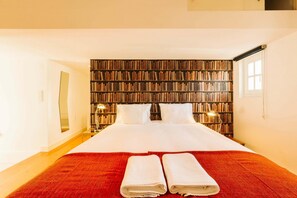 Une chambre d’hôtel avec un grand lit, un mur entier recouvert d’étagères et deux lampes de chevet.