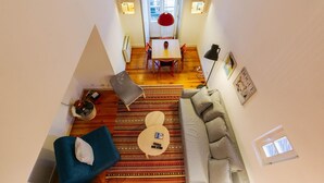 Un apartamento tipo loft con techo alto, un comedor con mesa y sillas rojas, un sofá, una mesa de centro y una alfombra estampada.