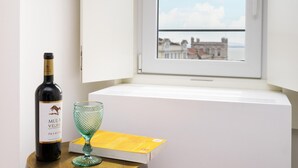 A bottle of Mula Velha Premium wine, a glass, and a book on a table by a window with a view of buildings and a bridge. - Velvet Dream SJ in Lisboa Ciudad (Lisbon)