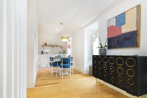 Een moderne keuken met witte kasten, een eetgedeelte met blauwe stoelen, en een zwarte console met ronde patronen.