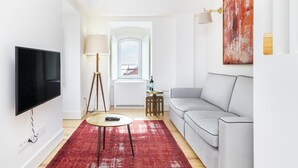 A modern living room with a flat-screen TV, a grey sofa, a red patterned rug, a small round table, and a floor lamp. - Velvet Dream SJ in Lisboa Ciudad (Lisbon)