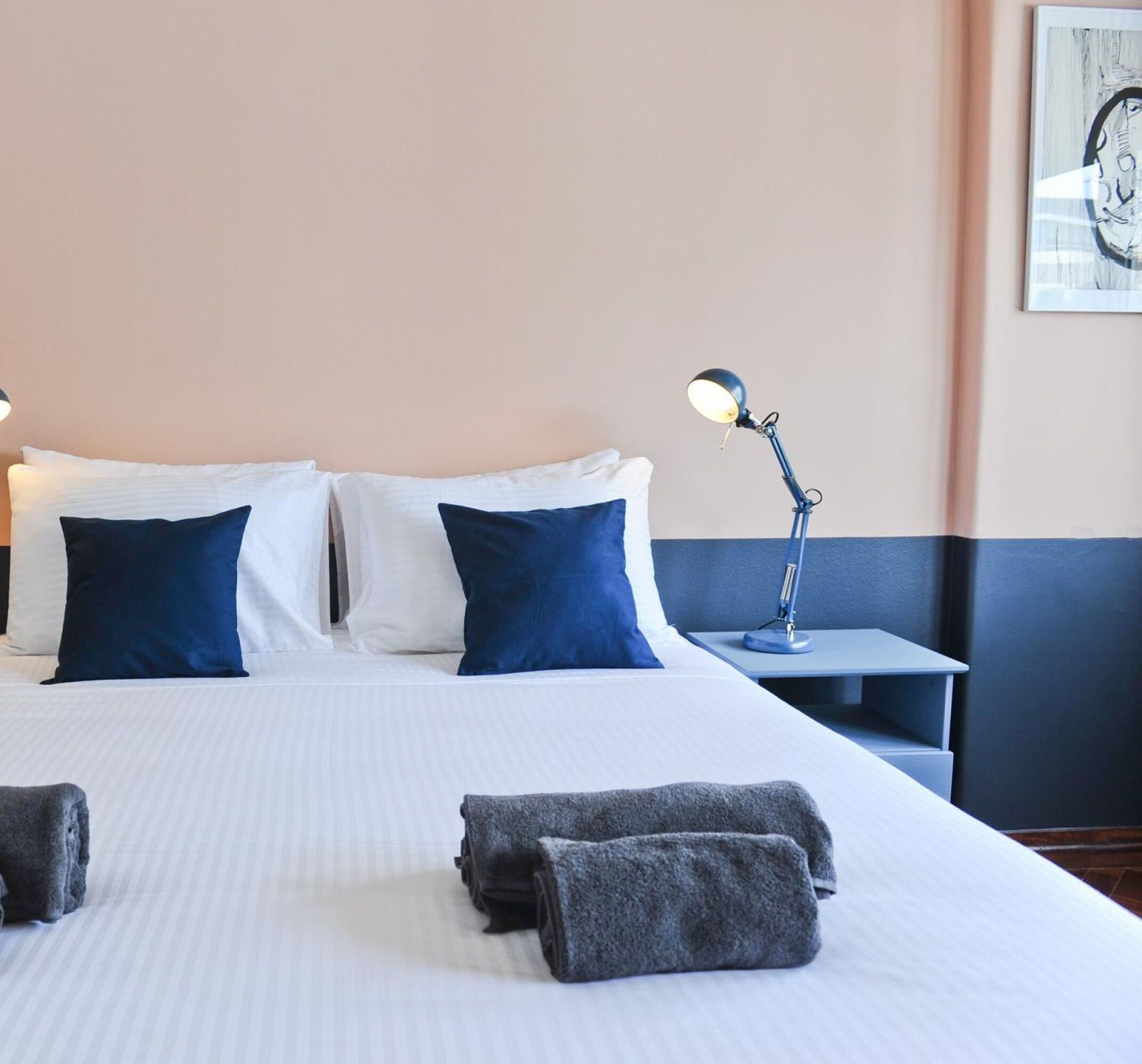 A neatly made bed with white and blue bedding, a bedside lamp, and a folded towel on the bed.