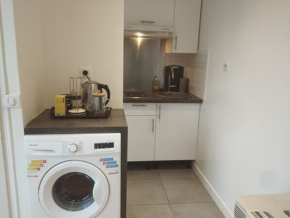 A compact kitchen with a washing machine, a coffee maker, and a kettle on the countertop.
