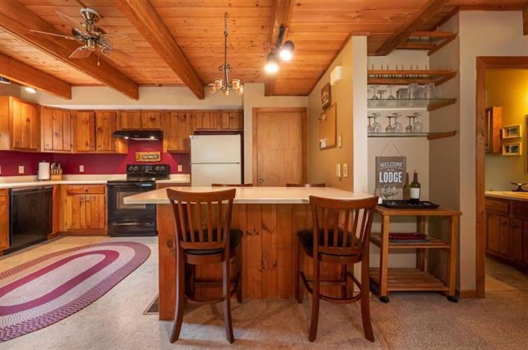 Una cocina con armarios de madera, una isla central con sillas, un refrigerador y un letrero que dice 'Welcome to the Lodge'.