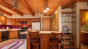 Een keuken met houten kasten, een centraal eiland met stoelen, een koelkast en een bordje met de tekst 'Welcome to the Lodge'.