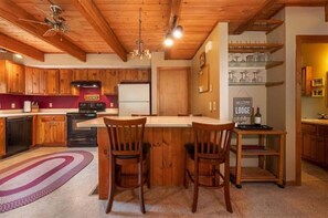 Une cuisine avec des meubles en bois, un îlot central doté de chaises, un réfrigérateur et une pancarte sur laquelle on peut lire : « Bienvenue au Lodge ».