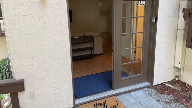 A residential entrance with a sliding glass door, a doormat with "yay! you're here!" text, and a number "2AL" on the door.