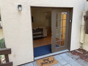 A residential entrance with a sliding glass door, a doormat with "yay! you're here!" text, and a number "2AL" on the door.
