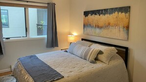 A bedroom with a bed, a window, a painting, and a lamp.