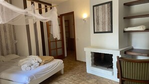 Un dormitorio con cama, chimenea blanca, una silla de madera y un armario.