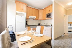 A compact kitchen with wooden cabinets, a microwave, and a dining area set for four with a table, chairs, and a small refrigerator.