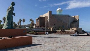 A plaza with a statue, a building with a dome, and palm trees. - Atamanja Beach Apatment Playa de Las Canteras (Palmas De Gran Canaria, Las)