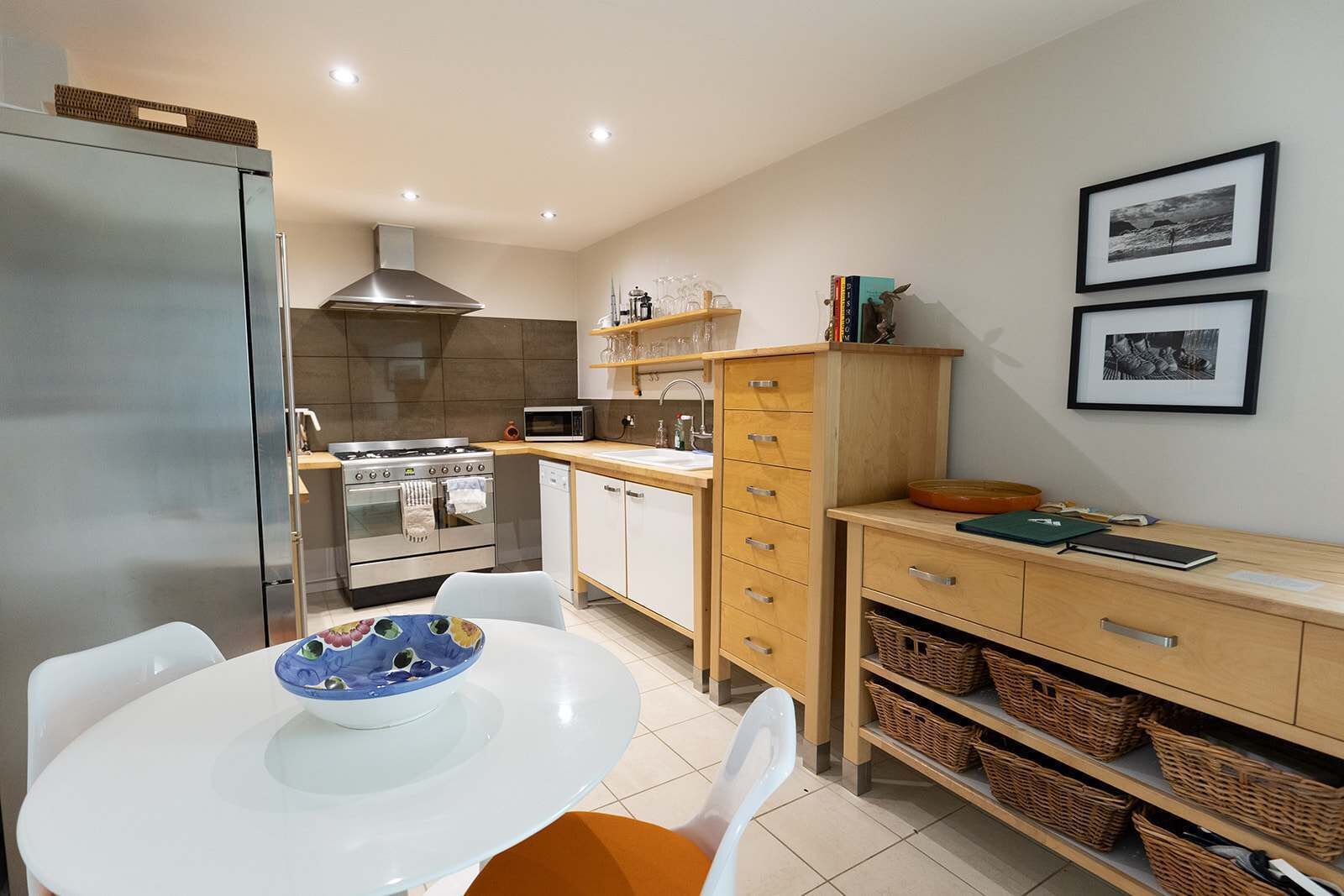A compact kitchen with modern appliances, a dining table with chairs, and a wooden cabinet with baskets.