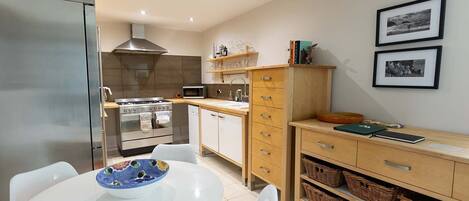 A compact kitchen with modern appliances, a dining table with chairs, and a wooden cabinet with baskets.