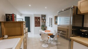 A modern kitchen with a refrigerator, a dining table with chairs, and a built-in bookshelf. - Beautiful Two Bedroom Cottage with Amazing Views (Birdsedge)
