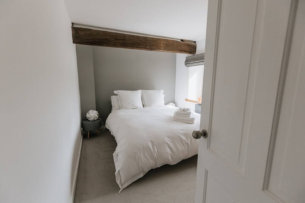 A bedroom with a bed, a bedside table, a window with curtains, and a door.