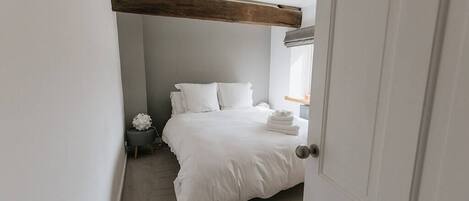 A bedroom with a bed, a bedside table, a window with curtains, and a door.