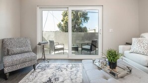 A living room with a sofa, armchair, and a coffee table with a plant. There is a sliding glass door leading to an outdoor area with chairs and a table. - 4046 · Modern condo in Hillcrest/Mission Hills (San Diego)