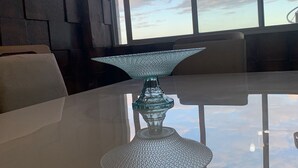 Ein moderner Essbereich mit einem Glastisch, einer dekorativen Glasdekoration und Blick auf den Himmel durch große Fenster.