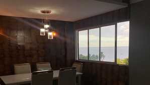 Ein modernes Wohnzimmer mit großem Fenster und Meerblick, einer Essecke mit Tisch und Stühlen sowie einer gemütlichen Sitzecke mit Sofa.