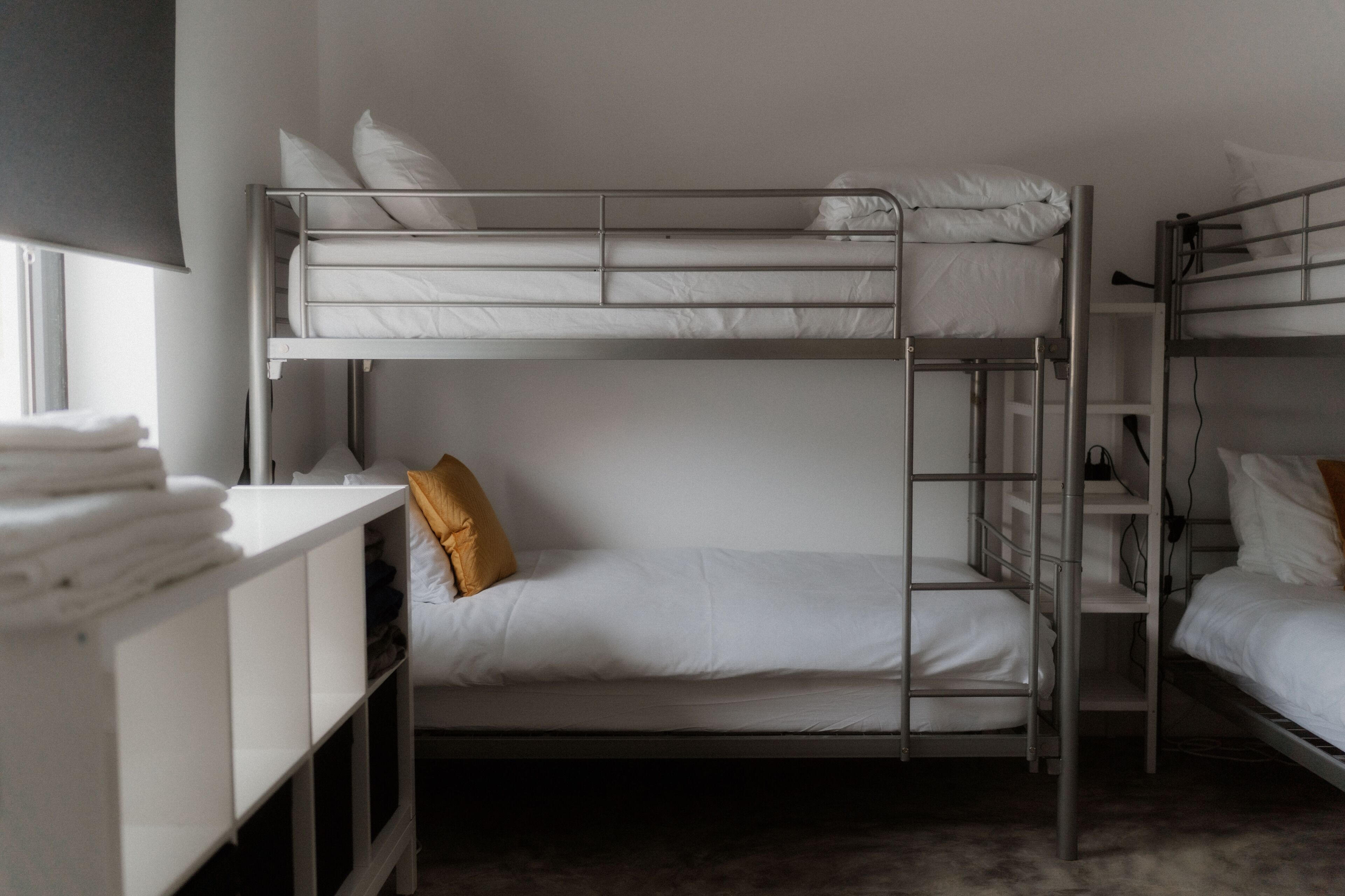 Une chambre avec un lit superposé, une échelle, du linge de lit blanc et une étagère avec des serviettes pliées.