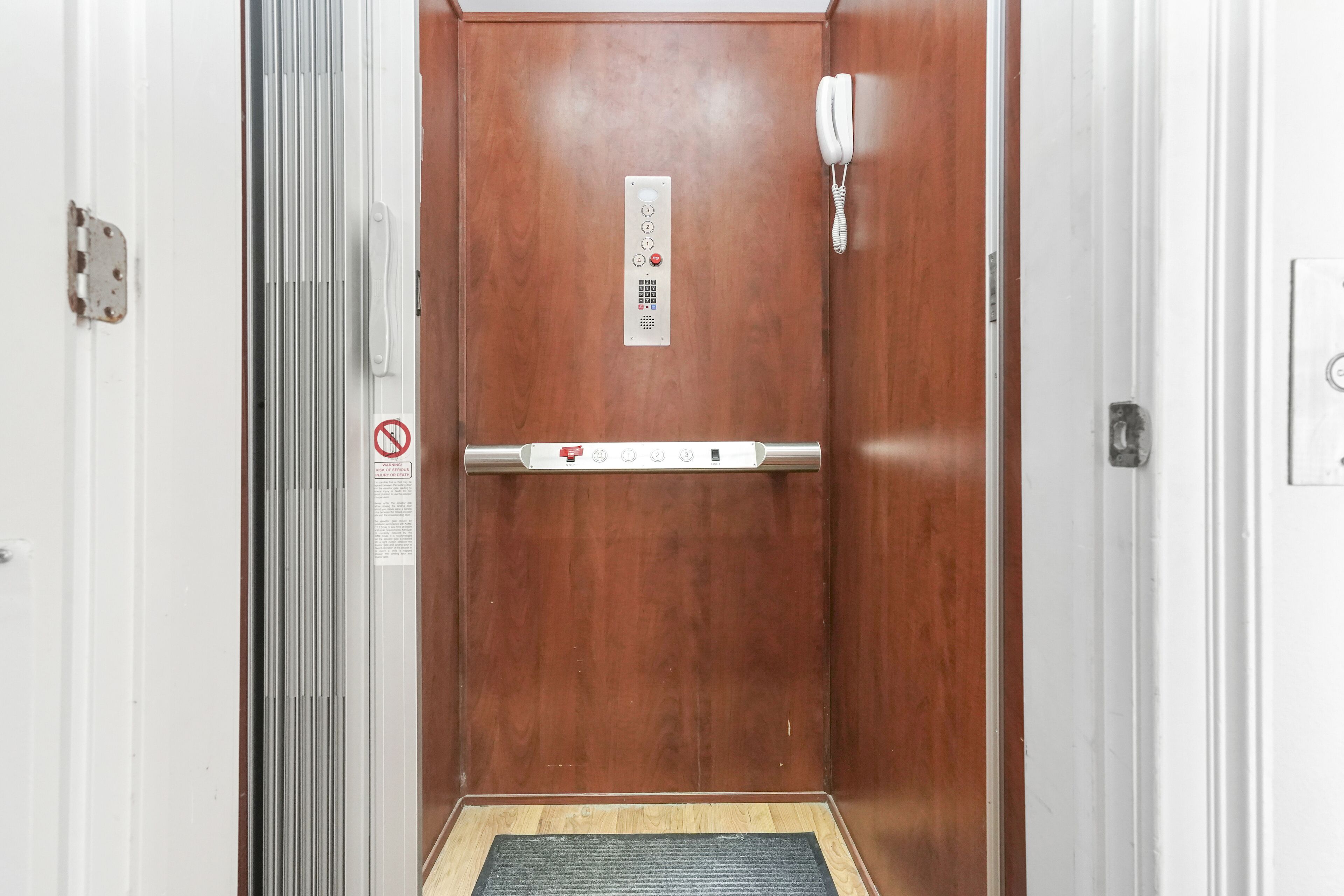 An elevator with a control panel, a phone, and a no-smoking sign.