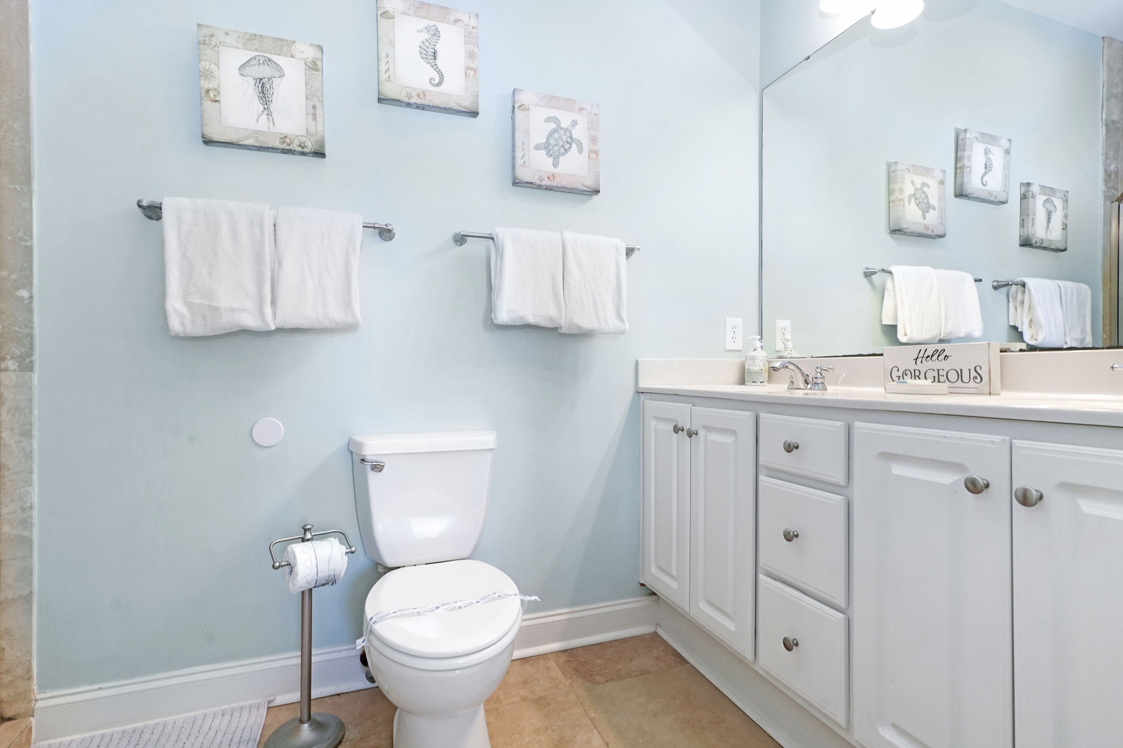 A bathroom with a toilet, white cabinets, and towels on towel racks.