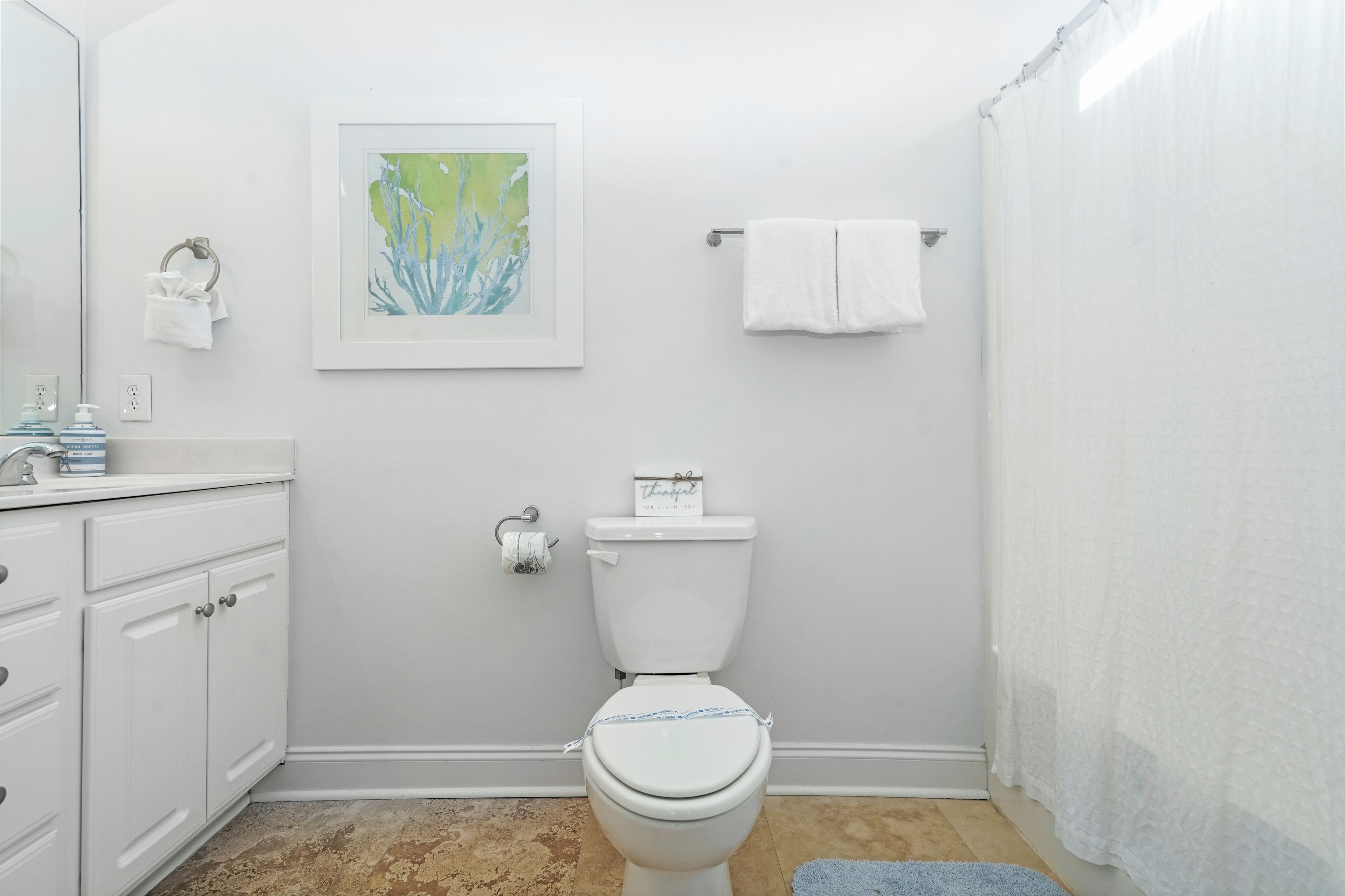 Een badkamer met toilet, wastafel, spiegel, een ingelijste foto en een handdoekhouder.