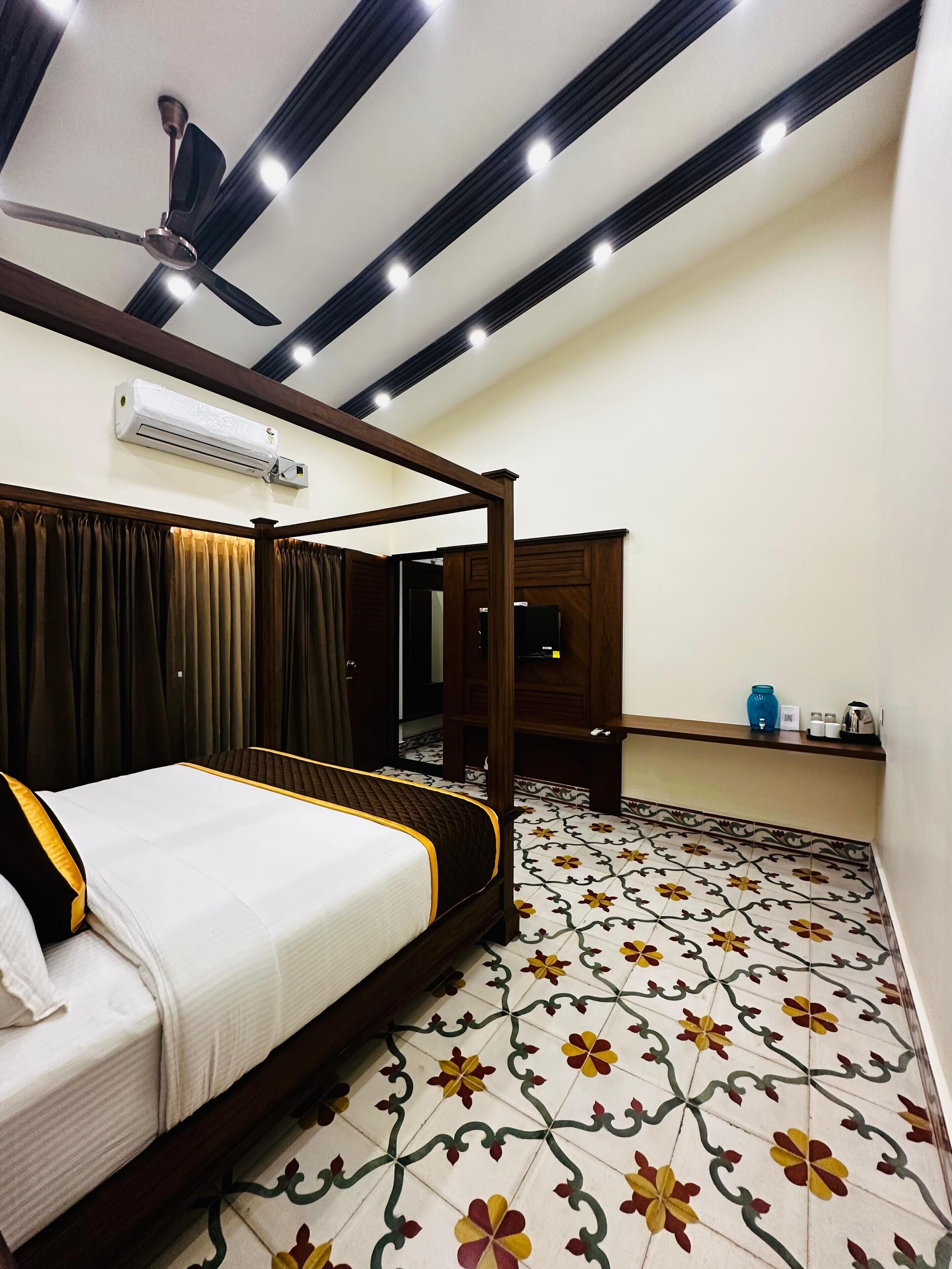 A bedroom with a four-poster bed, an air conditioning unit, a ceiling fan, a small cabinet, and a tiled floor with a floral pattern.