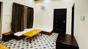 A room with a bed, a wooden table, a bench, a fan, and a black door. - Singaras Coffee Country (Ootacamund)