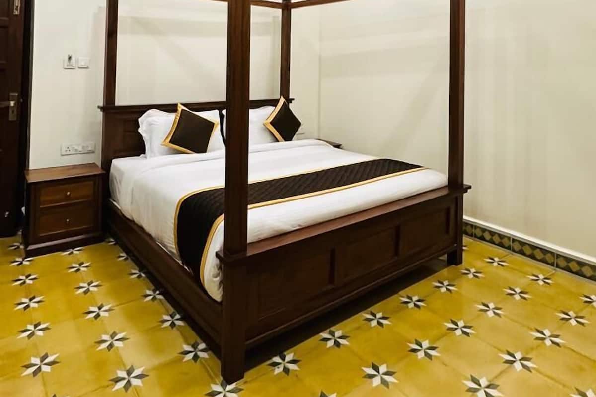 Ein Bett mit Baldachin, dessen Holzbettgestell mit weißer Bettwäsche bezogen ist, ein Deckenventilator und ein strukturierter Boden.