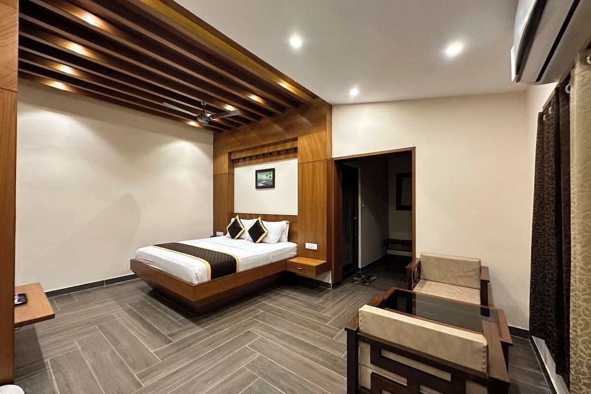 Ein modernes Hotelzimmer mit einem Holz-Kopfteil, einem Bett mit weißer und brauner Bettdecke, einem Holztischchen, einem kleinen Schreibtisch und einem Stuhl.