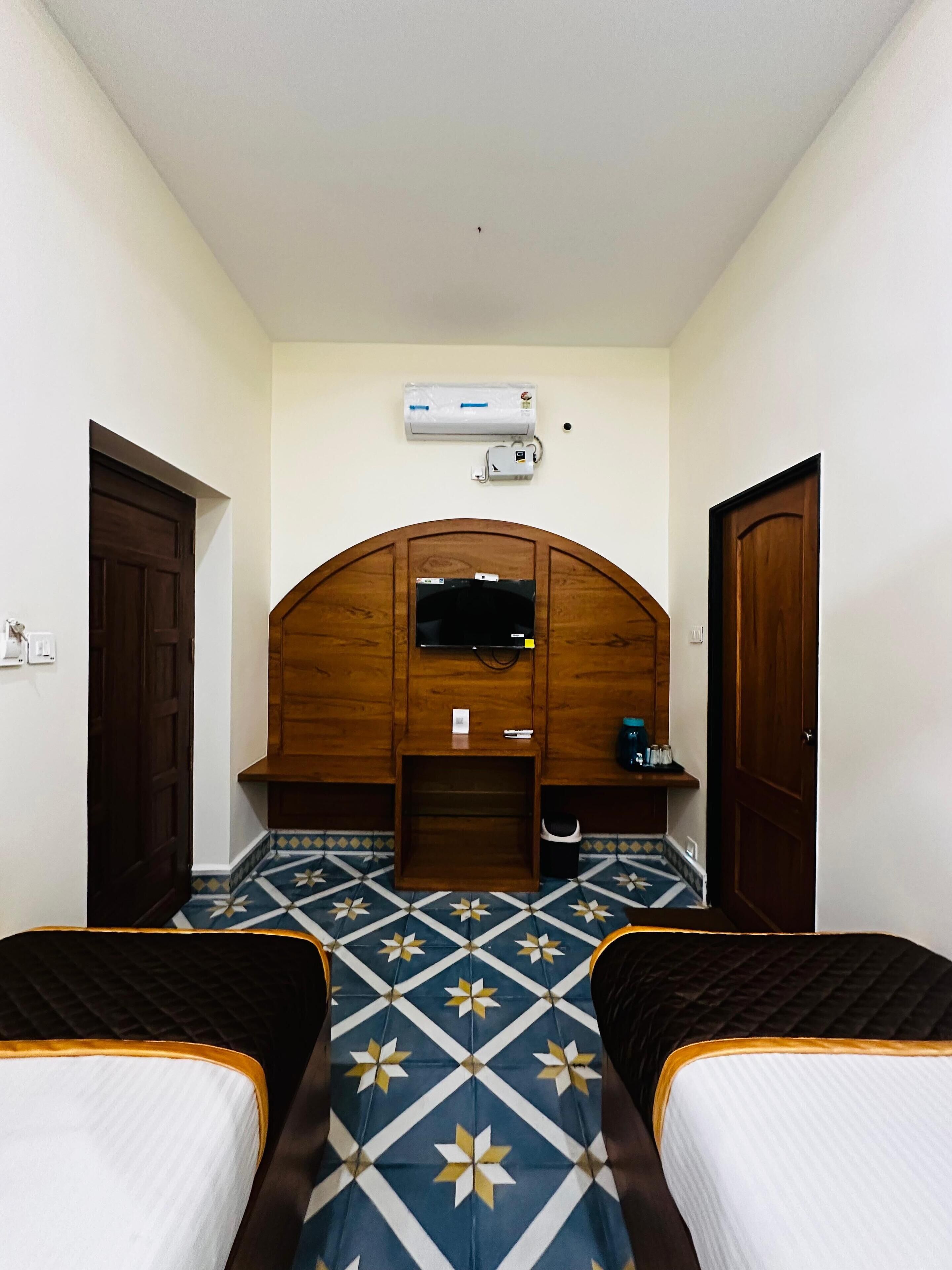A hotel room with two beds, a wooden headboard, a television, an air conditioning unit, and a tiled floor.