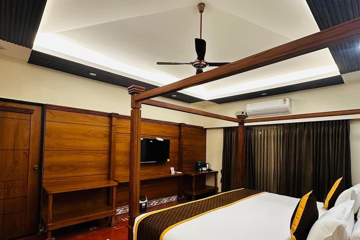 Ein Hotelzimmer mit einem hölzernen Himmelbett, einem Deckenventilator, einem Flachbildfernseher und einer Minibar.