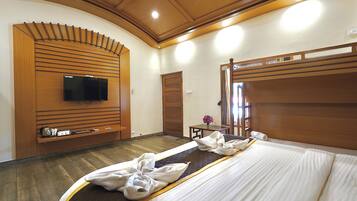 Habitación de hotel con una cama grande, cabecera de madera, un televisor de pantalla plana montado en la pared y una mesita con un jarrón de flores.