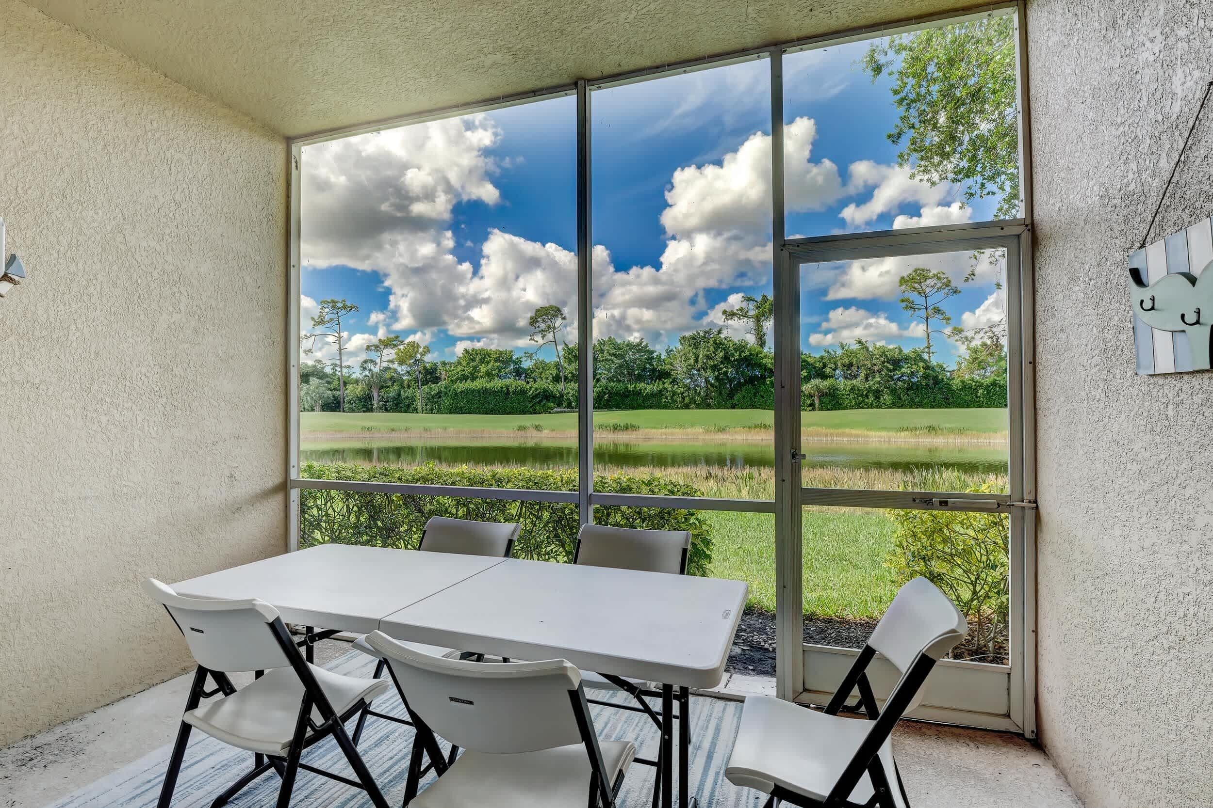 A conservatory with a table and chairs, large windows offering a view of a green landscape.