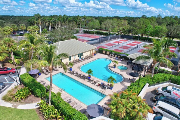 A resort with a large swimming pool, tennis courts, and a parking area.