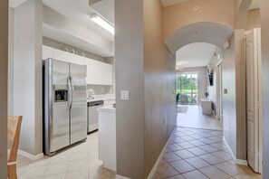 A modern kitchen with a stainless steel refrigerator, white cabinetry, and a tiled floor.