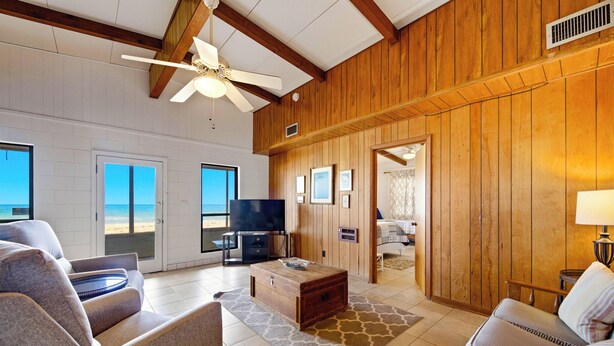 A spacious living area with a large TV, wooden walls, and a view of the beach.