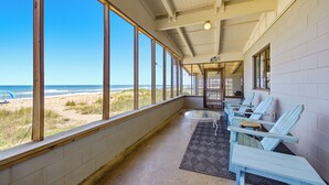 A covered porch with large windows overlooking the beach, light blue Adirondack chairs, and a small round table.