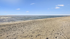 A wide sandy beach with footprints, a clear blue sky, and calm ocean waves.