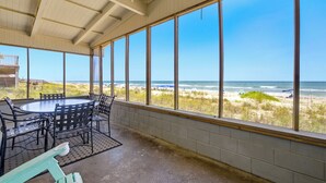A covered patio with a view of the beach, a round table, and chairs.