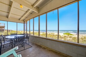 Eine überdachte Terrasse mit Blick auf den Strand, einem runden Tisch und Stühlen.