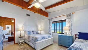 A bedroom with a bed, bedside tables, a dresser, a window with curtains, and a ceiling fan.