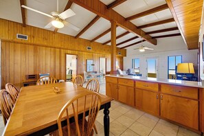A spacious dining area with wooden tables and chairs, a kitchen with wooden cabinets, and a ceiling fan.