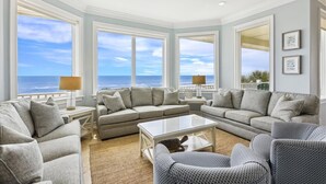 A spacious living room with a large window overlooking the ocean, a comfortable gray sofa set, a coffee table, and a patterned armchair. - Welcome to Aisle of Palms! (St. George Island)
