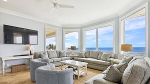 A spacious living room with a large flat-screen TV, multiple seating areas, and large windows offering a view of the ocean. - Welcome to Aisle of Palms! (St. George Island)