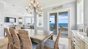 A dining area with a wooden table and wicker chairs, a chandelier, and a view of the ocean through a glass door. - Welcome to Aisle of Palms! (St. George Island)